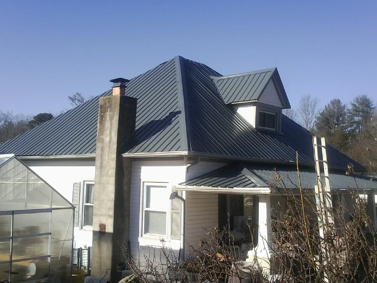 Dark blue standing seam metal roof on a white farmhouse with dormer — Slate & Tile Roof Repair by Roofing Brothers in Edgemoor