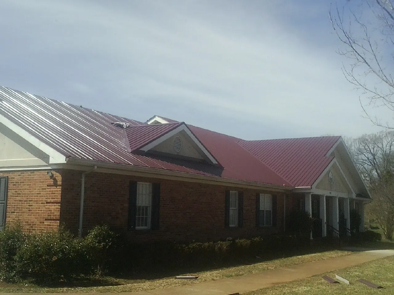 Red metal roof with gabled entries on a long brick building, from a Hail Damage Roof Repair job in Edgemoor