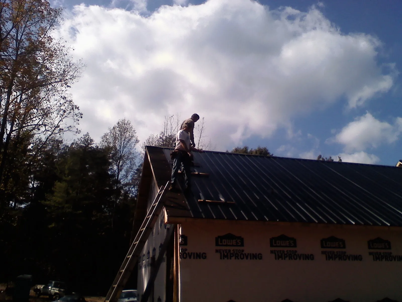 Roofer fastening dark metal panels high against a cloudy sky, from a Roof Inspection job in Edgemoor