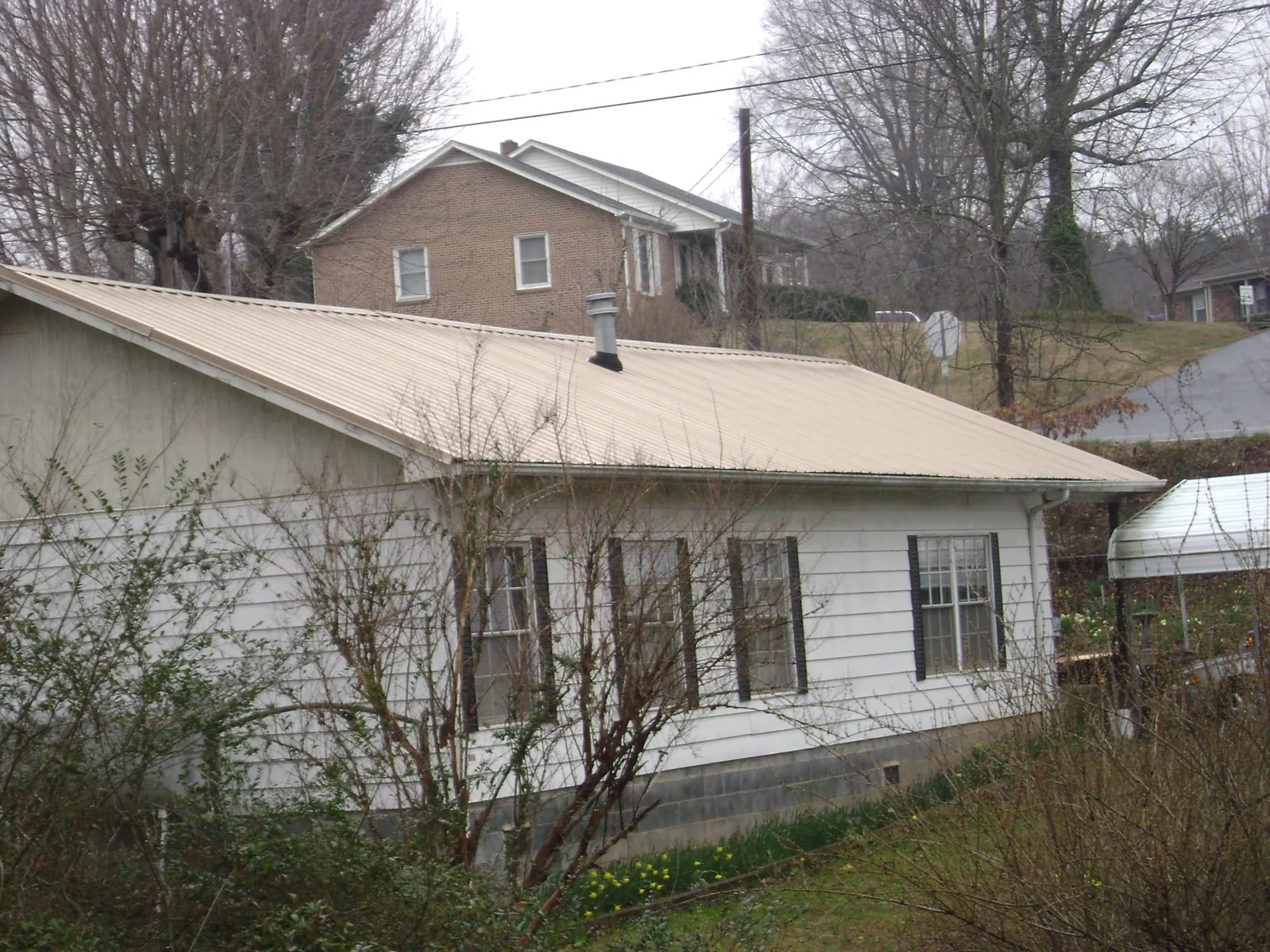 Tan metal roof on a white sided house set into a hillside — Commercial Roofing by Roofing Brothers in Edgemoor